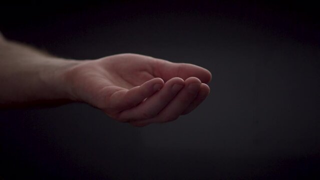 Slow motion water droplets falling in open caucasian hand on black background
