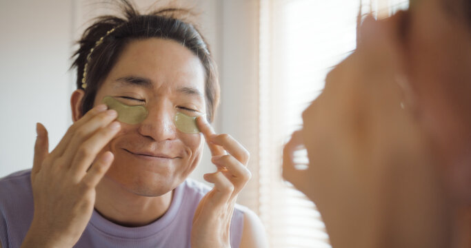 Gay queer man non-binary beauty blogger makeup artist at home cross dressing up apply face skin care eye make up brush. Real asia LGBT young guy adult people happy relax smile looking at mirror pride.