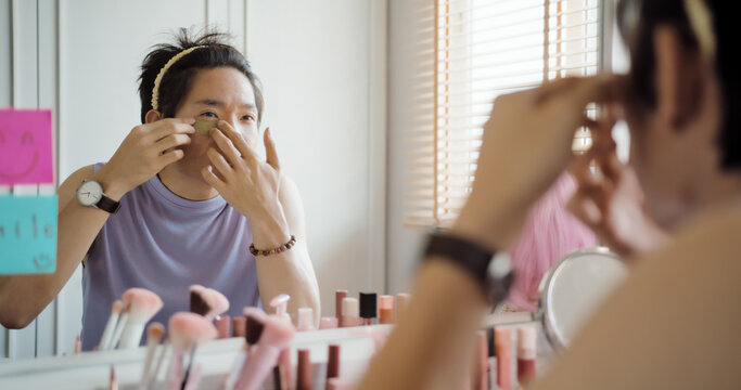 Gay queer man non-binary beauty blogger makeup artist at home cross dressing up apply face skin care eye make up brush. Real asia LGBT young guy adult people happy relax smile looking at mirror pride.