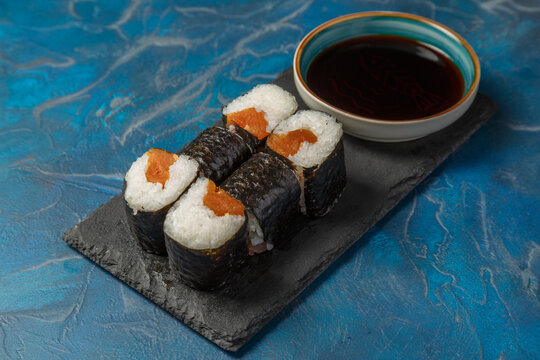 Maki au saumon- sp&eacute;cialit&eacute; culinaire japonaise - sur une ardoise avec une sauce soja et baguettes.