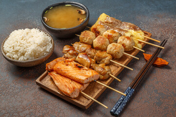 Assortiment de Yakitori japonais au saumon, au boeuf fromage, au poulet sur une ardoise. Servi avec une soupe miso et du riz. Menu.