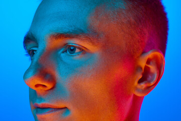 Close Up side view portrait of young handsome calm guy, student isolated on blue background in red neon light, filter. Confident, serious man.