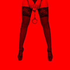 Beautiful woman body legs in high heels holding handcuffs in red light, BDSM - obrazy, fototapety, plakaty