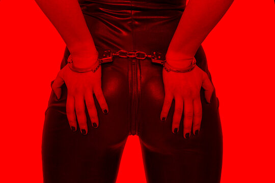 Sexy dominatrix hands on ass in handcuffs in red light, bdsm.