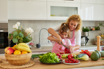 Mother teaching her daughter to cut vegetable in the kitchen at home
