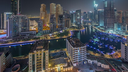 Naklejka premium Dubai Marina with several boat and yachts parked in harbor and skyscrapers around canal aerial all night timelapse.