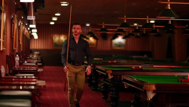 A young man plays American billiards. Russian billiards, an American in a billiards club and bar. Dark colors in the billiard club. A man pockets snooker balls.