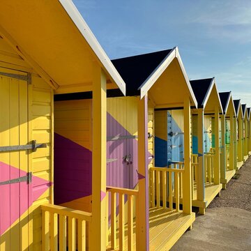 Row of multi coloured wooden beach huts on beach, Folkestone, Kent, England, UK