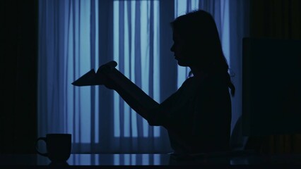Everyday life creative concept. Closeup shot of woman working at the desk at home in the dark room, reading documents.