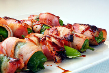 Padron pepper rolls wrapped in bacon on a white plate