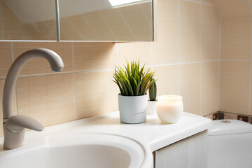 Using artificial flowers in bathroom interior at home. Potted flower plant on bathroom sink corner with candle burning.