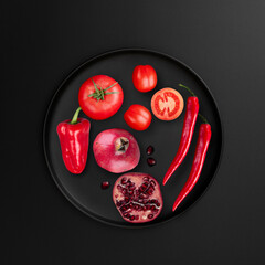 Red food items with tomato, pomegranate, red chilly pepper on black background, top view