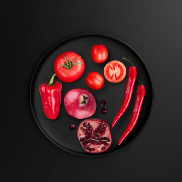 Red food items with tomato, pomegranate, red chilly pepper on black background, top view