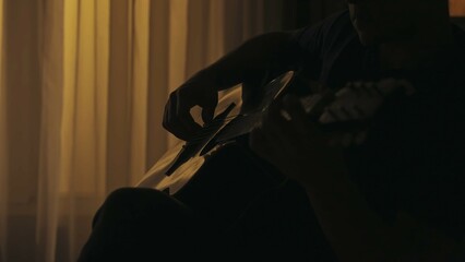 Closeup shot of a man sitting, playing melody on the acoustic guitar. Everyday life creative concept.