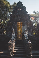 Porte dorée entourée de statues au temple bouddhiste Goa Lawah, Bali. Indonésie.