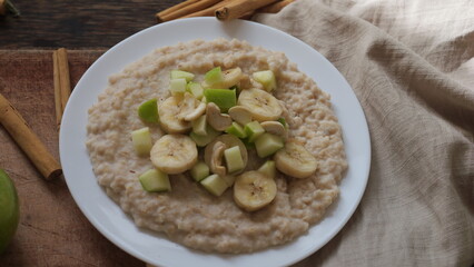 Plate of oatmeal porridge with green apple, cashew and banana. Close up.