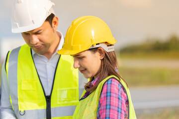 Close-up photo of Asian female engineer as manager Near a male engineer We are working on the business industry together with diligence. Wear a hard hat and vest. There's sunlight.