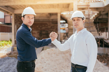Half-body photograph of Two Asian male engineers hold hands and work together. Powerful in construction projects related to the architectural industry. Wear a safety helmet and uniform.