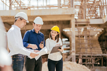 Construction project has a team of 3 male and female engineers, Asians, looking at architectural...