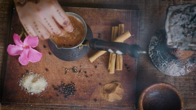 Indian woman hands add spices and sugar to masala chai tea making.