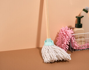 A metal basket with cleaning supplies, a pink rag to clean the floor and a mop. Copy space for text.