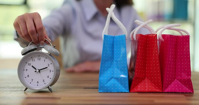 Woman buyer places alarm to remind about sale in shopping centres. Female puts vintage clock next to shopping gift bags slow motion