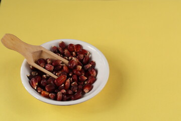 A Close up picture of a few Red Corn or Maize seeds used as a food ingredient against a light yellow colored background.