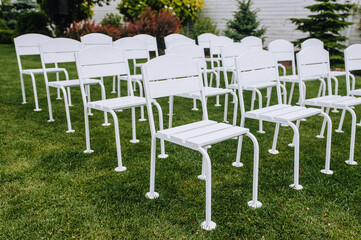 Beautiful white wooden chairs stand in a row on the green grass of the meadow.