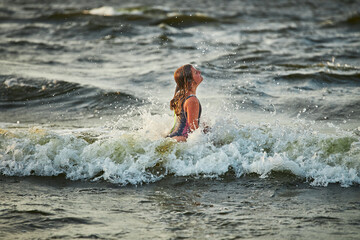Little girl playing with waves in the sea. Kid playfully splashing with waves. Child jumping in sea waves. Summer vacation on the beach