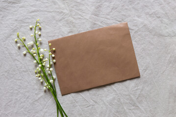 Blank greeting card, invitation and envelope mockup. Minimal floral arrangement with white lilies of the valley. Flat lay, top view. Happy mother's day, birthday, wedding composition.