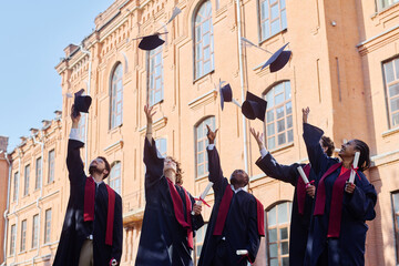 Graduated students throwing their hats while standing outdoors against the university