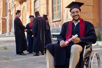 Portrait of student with disability sitting on wheelchair and smiling at camera, he graduating from...