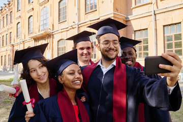Happy graduated students having video call on smartphone while standing outdoors