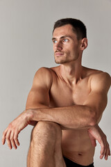 Portrait of handsome young man with grey eyes, posing shirtless against grey studio background. Muscular body. Concept of men's health and beauty, body care, fitness, wellness, ad