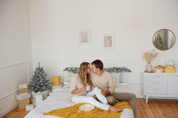 Cute, cheerful couple cuddling on bed with yellow blanket on Christmas. Tender woman and young man...