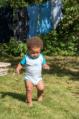 A toddler runs around on the grass. A young biracial boy has fun playing in the garden.