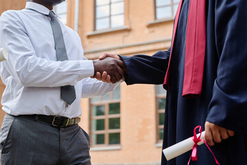 Close-up of African American teacher shaking hands with student, he congratulating him with graduation