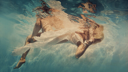 A woman in white swims underwater as if flying in zero gravity - obrazy, fototapety, plakaty