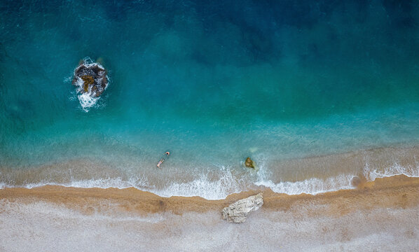 Aerial view of a couple of guys swimming in crystal clear water illuminated by sunlight close to an empty beach, Cala Moraig, Zona Encinas, Cumbre del Sol, Alicante, Spain.