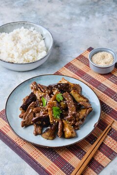 Chinese style beef with eggplant on a gray plate on a light concrete background. Served with boiled rice. Beef recipes.