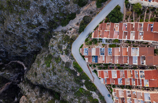 Aerial view of a lively townscape with organized architecture divided from a cliff by an asphalt road, Zona Encinas, Cumbre del Sol, Alicante, Spain.