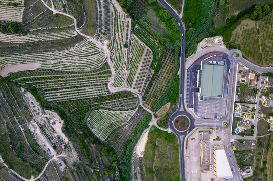 Aerial view of a serpentine road and a modern building complex, close to green agricultural fields, Zona Encinas, Cumbre del Sol, Alicante, Spain.