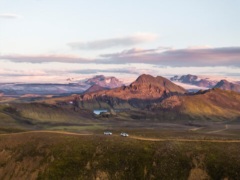 Aerial view of cars stopped along the road on the hill crest with beautiful mountain landscape at sunset and Alftavatn Lake in foreground, Hella, Southern Region, Iceland.