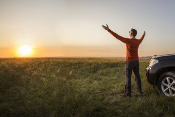 happy man tourist with open arms near his car at summer fieid at dawn or sunrise. Summer vacation adventure freedom auto travel concept.