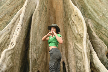 Fototapeta premium Pretty Asian woman Cheerful and happily at the base of a big tree. And this tree is very large and is a popular attraction for Thai tourists. Located at Uthai Thani Province in Thailand.