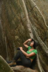 Pretty Asian woman sitting and resting after tired walking. at the roots of a big tree This tree is very large and is a popular attraction for Thai tourists. Located at Uthai Thani in Thailand.