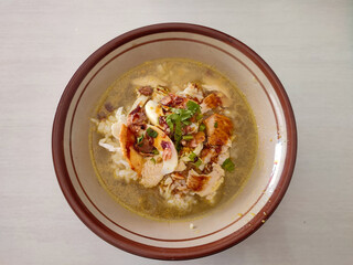 Simple soto ayam in a bowl with cream background.  Soto ayam is a typical Indonesian food, a type of chicken soup with a yellow broth because it contains turmeric.