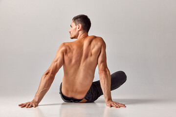 Man with muscular, strong, relief body posing shirtless in jeans against grey studio background. Back view. Concept of men's health and beauty, body care, fitness, wellness, ad