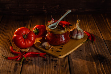 Red tomatoes and peppers on wooden table with adjika and ketchup in jar
