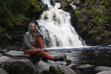 Fototapeta na wymiar a young beautiful woman tourist sitting against the backdrop of a waterfall surrounded by forest